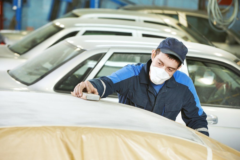 professional repairman worker in automotive industry sanding metal caer roof before painting at bodywork