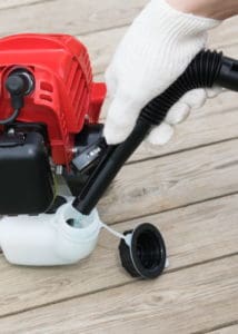 hand in a glove pours gasoline into a tank of a red lawn mower, closeup view