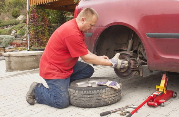 image of man in red shirt changing the brakes on a car. 